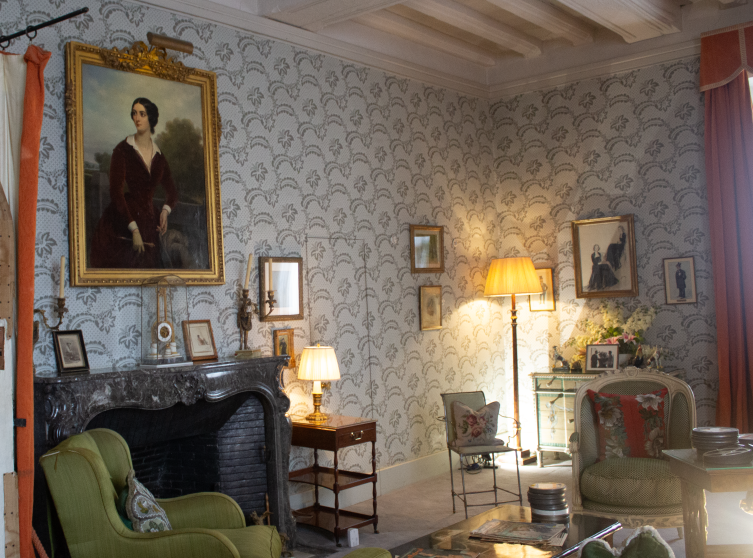 Salon avec fauteuils verts, plusieurs tableaux sur les murs, lampadaires allumés